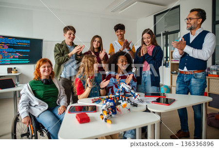 Group of high school students celebrating successful experiment with robotic hand. 136336896