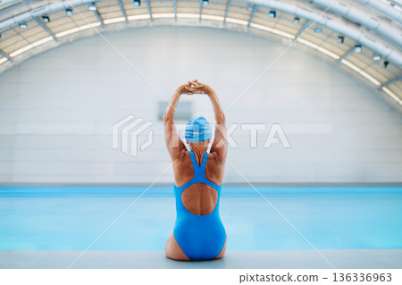 Rear view of female swimmer stretching before swim in pool. 136336963