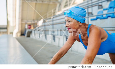 Older female swimmer stretching before swim in pool. Older female swimmer stretching before swim in pool. 136336967