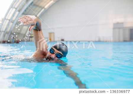 Focused swimmer performing crawl stroke in water. 136336977