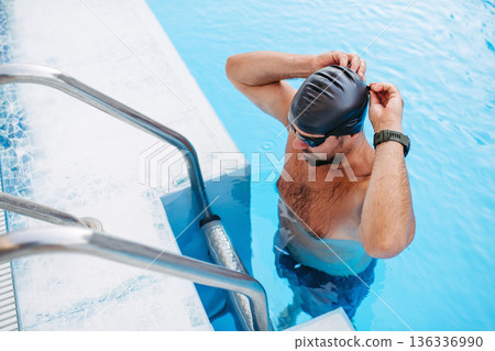 Male swimmer is preparing for swim in pool. Male swimmer is preparing for swim in pool. 136336990