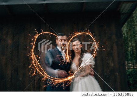 Bride and groom with sparklers creating a heart shape. Bride and groom with sparklers creating a heart shape. 136336992