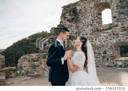 Bride and groom dancing, looking at each other. Wedding couple standing outside near ruins. 136337018