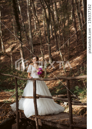 Bride in a snow-white wedding dress in nature, surrounded by a forest. Bride in a snow-white wedding dress in nature, surrounded by a forest. 136337162
