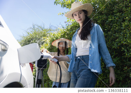 Tennage Girls EV charging an electric car. Power supply for electric car charging. Tennage Girls EV charging an electric car. Power supply for electric car charging. 136338111