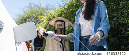 Tennage Girls EV charging an electric car. Power supply for electric car charging. Tennage Girls EV charging an electric car. Power supply for electric car charging. 136338112