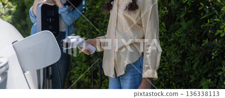 Tennage Girls EV charging an electric car. Power supply for electric car charging. Tennage Girls EV charging an electric car. Power supply for electric car charging. 136338113
