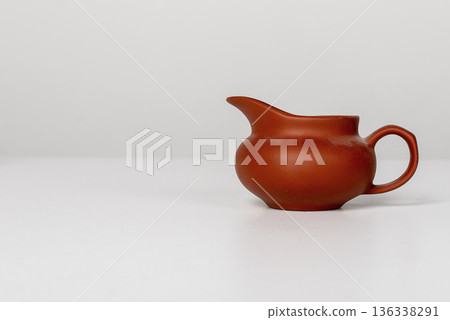 Small ceramic creamer, small jug, little pitcher with a rounded body, side handle placed on table. 136338291