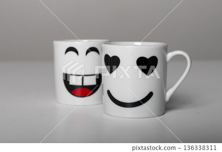 Two white ceramic mugs with playful emoji faces. Cute smiling happy and valentine love cup designs, Two white ceramic mugs with playful emoji faces. Cute smiling happy and valentine love cup designs, 136338311