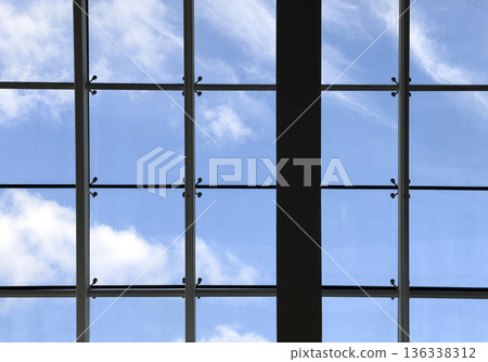Upward view of a modern glass roof with metal framing against a blue sky with soft clouds. Clean Upward view of a modern glass roof with metal framing against a blue sky with soft clouds. Clean 136338312