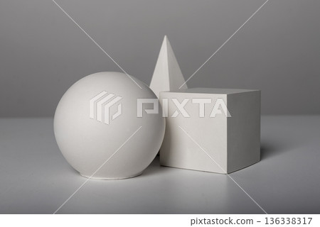white geometric shapes including a sphere, cube, and pyramid arranged on a neutral surface. Clean white geometric shapes including a sphere, cube, and pyramid arranged on a neutral surface. Clean 136338317