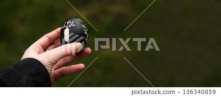 Black Easter egg in hand. Easter banner background. Defocus, blu 136340859