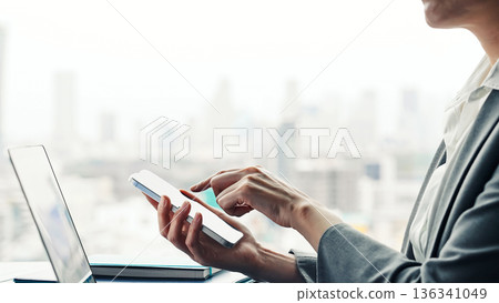 一位女性商務人士在城市辦公大樓內使用筆記型電腦和智慧型手機工作 136341049