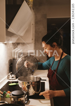 Woman Checking Food Readiness in Kitchen Saucepan 136341185