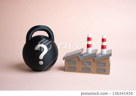 An industrial plant and a black weight with a question mark. Factors suppressing production and industry. Economic uncertainty theme. Business faces risks, market volatility and planning challenges. 136341450