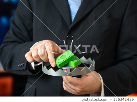 A businessman puts money bait into a trap. Investment traps. Concept of risky offers that lure investors. Visual metaphor about fraud schemes, hidden terms and the need for financial caution. 136341459