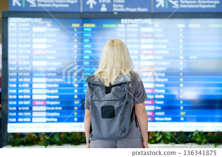 Traveling to new destinations as a woman checks the departure board at an airport, planning her next journey on a summer Thursday in July Traveling to new destinations as a woman checks the departure board at an airport, planning her next journey on a summer Thursday in July 136341875