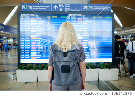 Traveler checking departure information at an airport in Malaysia during the day while carrying a backpack Traveler checking departure information at an airport in Malaysia during the day while carrying a backpack 136341876