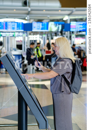 Traveler uses self-check-in kiosk at busy airport while preparing for upcoming flight to an international destination Traveler uses self-check-in kiosk at busy airport while preparing for upcoming flight to an international destination 136342084