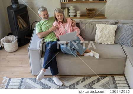 Older adults relaxing on couch looking at laptop screen 136342985