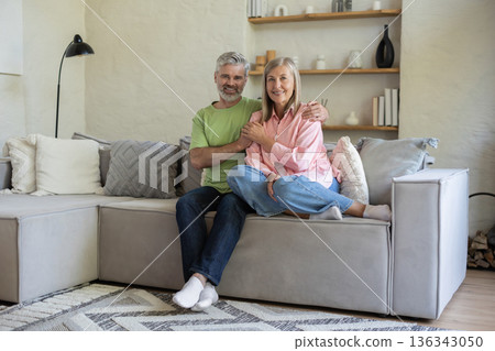 Adult couple sitting and embracing on sofa feeling coziness calm and tenderness Adult couple sitting and embracing on sofa feeling coziness calm and tenderness 136343050