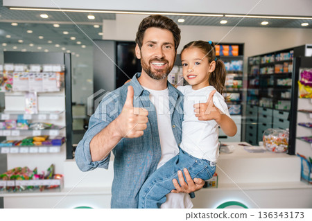 Father and daughter showing thumbs up while standing in pharmacy Father and daughter showing thumbs up while standing in pharmacy 136343173