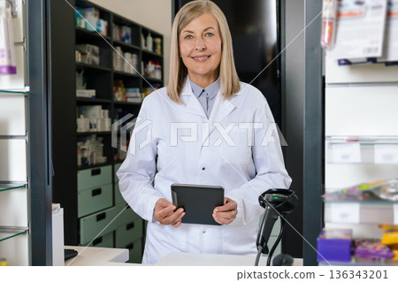 Mature blonde pharmacist looking contented while working in a drug store Mature blonde pharmacist looking contented while working in a drug store 136343201
