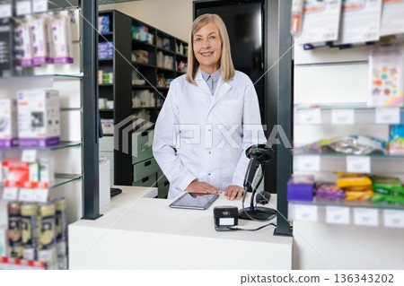 Mature blonde pharmacist looking contented while working in a drug store Mature blonde pharmacist looking contented while working in a drug store 136343202