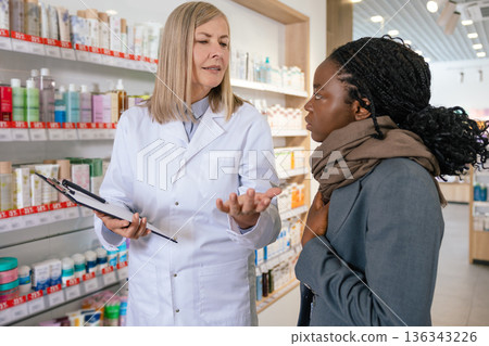 Sick african american girl talking to a pharmacist in a drug store Sick african american girl talking to a pharmacist in a drug store 136343226