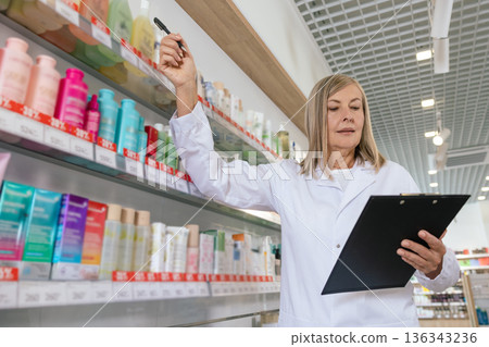 Blonde caucasian pharmacist doing inventarization in a drug store Blonde caucasian pharmacist doing inventarization in a drug store 136343236