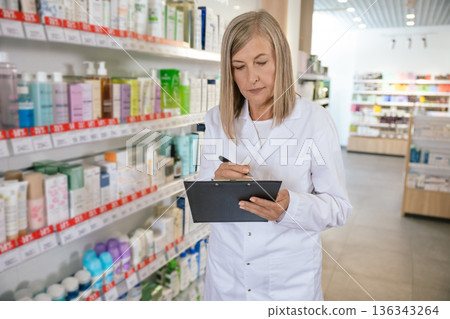Mature blonde pharmacist in a lab coat in a drug store Mature blonde pharmacist in a lab coat in a drug store 136343264
