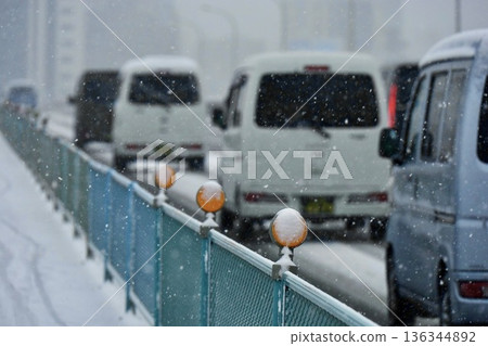 行駛中的汽車上積滿了雪,新荒川大橋上則有橘色的視覺引導標誌。 行駛中的汽車上積滿了雪,新荒川大橋上則有橘色的視覺引導標誌。 136344892