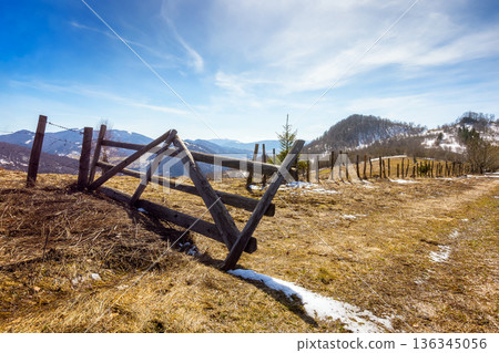 rural landscape of carpathian mountains in early spring under blue sky. snow covered hill with barbed wire fence on a sunny day. green environment sustainability and protection. background for earth 136345056