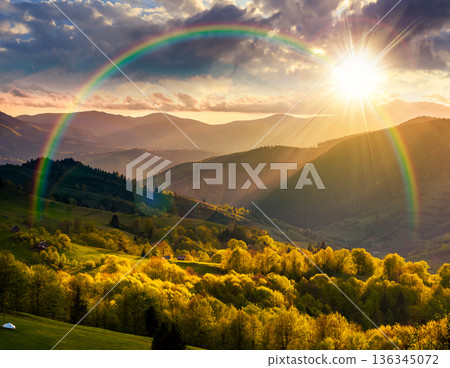gorgeous countryside in spring at sunset. beautiful mountain landscape with cloudy sky over the forested rolling hills in evening light. scenery with atmospheric weather and rainbow in highland vista 136345072