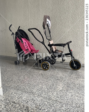 Two strollers parked next to a wall in a building hallway during daytime 136345123