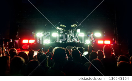 Crowd gathers for a live music performance in a venue with bright lights and a drum set on stage 136345164