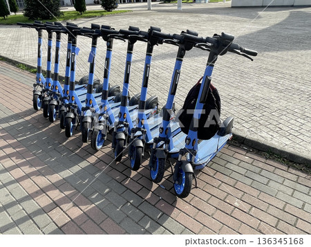 A row of scooters sits on the sidewalk for rent on a sunny day A row of scooters sits on the sidewalk for rent on a sunny day 136345168