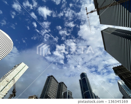 Tall buildings reach for the sky with clouds above in a city construction site during daylight hours Tall buildings reach for the sky with clouds above in a city construction site during daylight hours 136345169