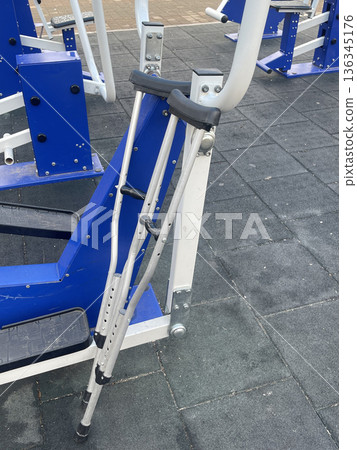 Metal crutches lean against blue gym equipment in a fitness area during the day 136345176