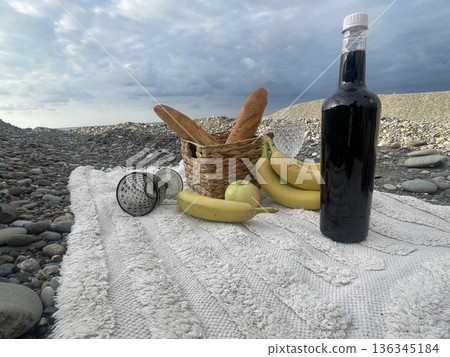 Empty beach scene with a picnic setup featuring bread, fruit, and a drink  136345184