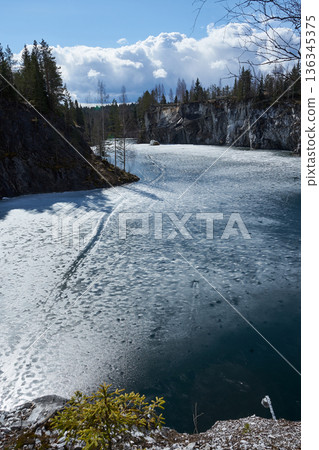 Ruskeala marble quarry in spring. Frozen lake surrounded by rock cliffs and pine forest. Tourism and nature landscape Ruskeala marble quarry in spring. Frozen lake surrounded by rock cliffs and pine forest. Tourism and nature landscape 136345375