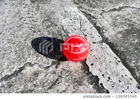 red plastic toy ball with white stripes on concrete ground with shadow 136345540