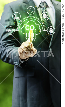 Businessman pointing at a glowing CO2 reduction cloud icon surrounded by green energy and sustainable transport symbols for environmental responsibility and net zero goals 136345764