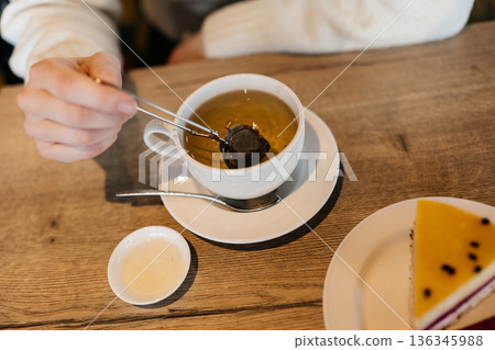 Enjoying tea and dessert at a cafe during afternoon hours with a hand holding a teabag Enjoying tea and dessert at a cafe during afternoon hours with a hand holding a teabag 136345988