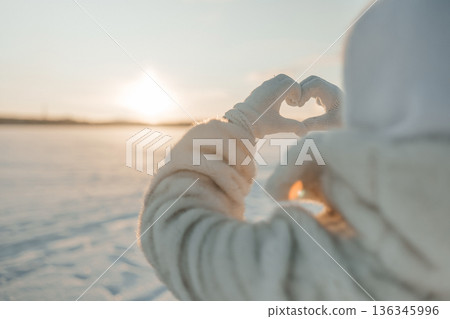 Making a heart shape with hands during sunset on a snowy landscape Making a heart shape with hands during sunset on a snowy landscape 136345996