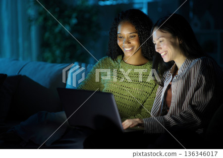 Two happy diverse friends checking laptop in the night 136346017