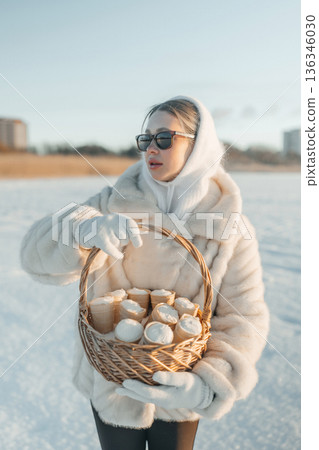 Woman carries basket of baked goods while standing in snow on a bright winter day 136346030