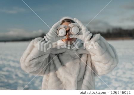 Person wearing a white coat looks through binoculars on a snowy field during daylight 136346031