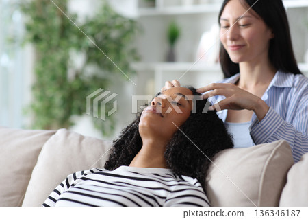 Asian woman massaging head of black female at home Asian woman massaging head of black female at home 136346187