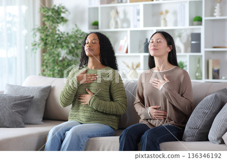 Two diverse friends doing breathing exercises at home Two diverse friends doing breathing exercises at home 136346192